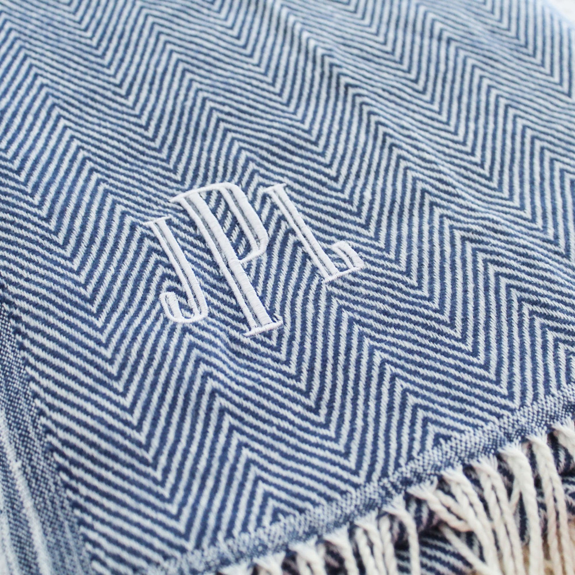 May include: A blue and white chevron patterned throw blanket with white fringe. The blanket has the initials 'J.P.L.' embroidered in white thread.